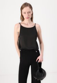 Svart sateng camisole med tynne stropper, paret med skreddersydde svarte bukser og en buet svart skinnveske. Glatt tekstur og minimalistisk design.