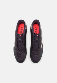 Zapatos de fútbol sintéticos negros con una textura suave, que cuentan con una punta redondeada, cordones centrales y detalles rojos en el revestimiento interior y el logo.