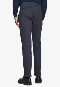 Dunkelgraue Hose mit geradem Schnitt, ausgestattet mit zwei aufgesetzten Gesäßtaschen, Gürtelschlaufen und umgeschlagenen Säumen, kombiniert mit schwarzen Schuhen.