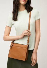 Brun läder crossbody-väska med rektangulär form, slät yta, justerbar rem och zip-up toppstängning.