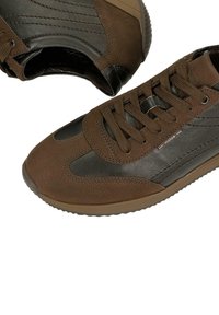 Hnědé tenisky vyrobené z texturované kůže a hladkých syntetických materiálů. Mají zakulacenou špičku, šněrovací design a gumovou podrážku s vzorkem.