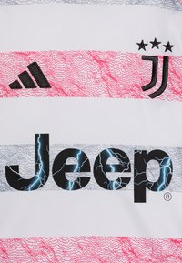 Maglia sportiva bianca con logo 'Jeep' nero audace e accenti a forma di fulmine, emblemma della Juventus, tre stelle e strisce a motivi rosa e grigio.