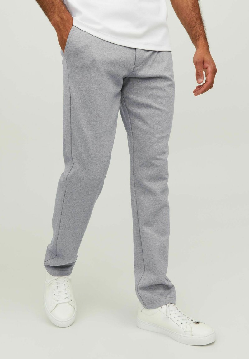 Graue Sweatpants aus weichem Material, mit geradem Schnitt, Seitentaschen und einer strukturierten Oberfläche. Kombiniert mit weißen Turnschuhen.