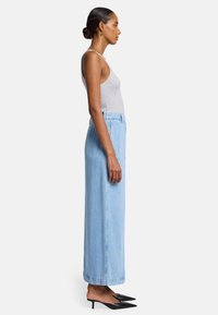 Lichtblauwe denim maxi-rok met een recht vallende pasvorm, hoge taille en zijzakken; gedragen met een grijze ribbel- tanktop en zwarte puntige hakken.