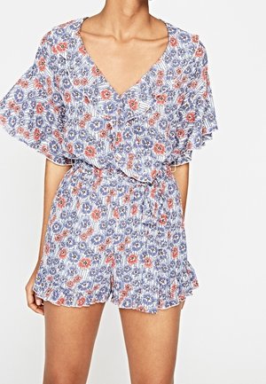 Combinaison fleurie en bleu, blanc et corail avec un décolleté en V, des manches évasées et un ourlet à volants. Confectionnée en tissu léger à motif texturé.