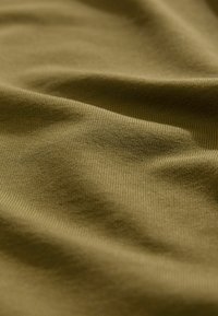 Olivovo zelená bavlnená tkanina s hladkým povrchom, ktorá sa vyznačuje jemným ryhovaním a miernymi záhybmi, zachytávajúcimi variácie svetla a tieňov.