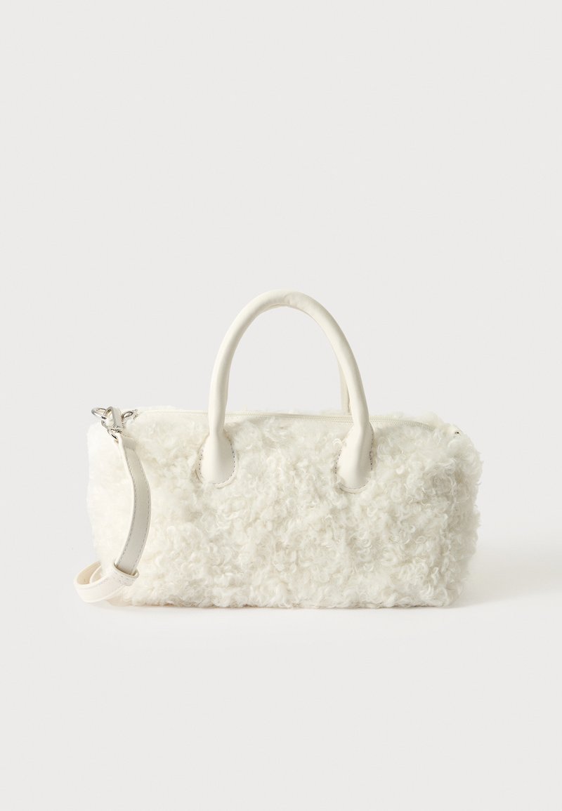 Petit sac à main blanc à texture de fourrure bouclée, doubles poignées et bandoulière amovible sur un fond clair uni.