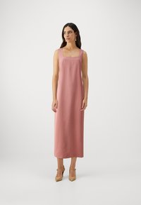 Roosa midi-kleid, millel on ruudukujuline kaelus ja laiad rihmad, valmistatud siledast kangast. Kandmisel beežid plokkninaga kingad, minimalistik disain.