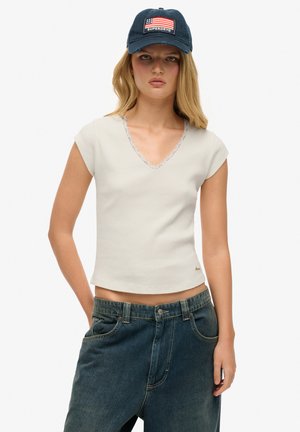 Crème fitted V-hals top met kantafwerking en korte mouwen, gecombineerd met hooggeposeerde donkerblauwe spijkerbroeken. Casual, gestructureerde uitstraling.