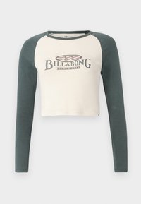 Maglietta a maniche lunghe accorciata con corpo crema e maniche raglan verde scuro. Presenta un classico logo Billabong stampato sul fronte.