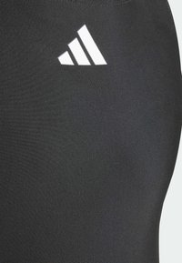 Zwarte sportlegging met een gladde textuur en een opvallend wit Adidas-logo nabij de tailleband. Ontworpen voor comfort en flexibiliteit.