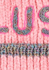 Gebreide roze stof met verhoogde, kleurrijke tekst en glanzende metallic accenten. Het onderste gedeelte toont een gevlochten textuur in verschillende kleuren.