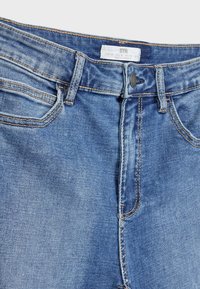 Modré džínové džíny s vysokým pasem, zapínáním na knoflíky vpředu a stylem s pěti kapsami, doplněné kontrastním šitím.