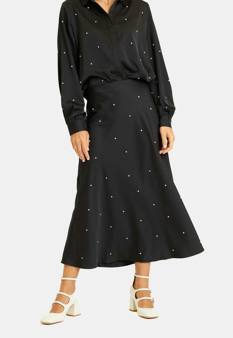 Blusa negra con cuello, mangas largas y adornos parecidos a perlas; combinada con una falda negra a media pierna a juego. Zapatos de tacón de bloque blancos.