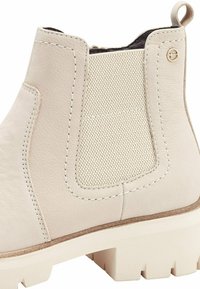 Botte de cheville en cuir beige avec panneau en tissu texturé, côté élastiqué, semelle blanche robuste et détail de couture contrasté.