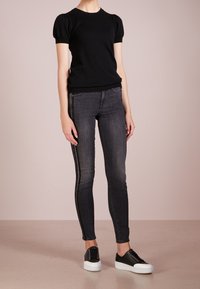 Czarny dzianinowy top z krótkimi bufkami, zestawiony z ciemnymi dopasowanymi dżinsami z bocznym paskiem. Uzupełniony czarnymi trampkami z białą podeszwą.