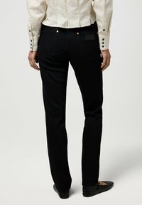 Jeans de mezclilla negra con un corte ajustado, que cuentan con bolsillos traseros con costuras en forma de V, remaches de cobre y un acabado suave y texturizado.