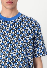 Kurzarm-T-Shirt mit einem geometrischen Muster in Blau, Schwarz und Weiß, mit einem einfarbigen blauen Rundhalsausschnitt und einer lockeren Passform.