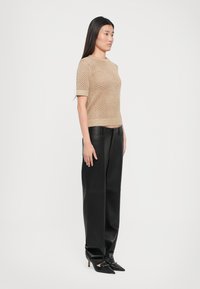 Maglione beige lavorato a maglia con maniche corte, caratterizzato da un tessuto a trama aperta. Abbinato a pantaloni in pelle neri a vita alta e tacchi a punta neri.