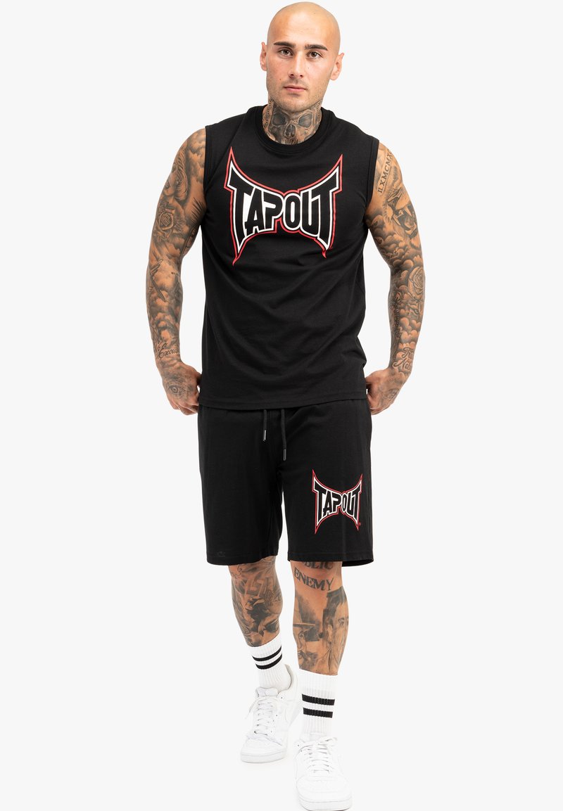 Juoda be rankovių marškinėliai ir atitinkamos šortai su raudonos ir baltos spalvos "TAPOUT" logotipu. Audinys atrodo kvėpuojantis, o siluetas – sportiškas. Balti sportbačiai ir dryžuotos kojinės.