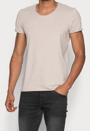 Hellbeige Kurzarm-T-Shirt mit rundem Ausschnitt, aus weichem Stoff, kombiniert mit dunklen Jeans, die einen lässigen Schnitt zeigen.