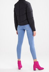 Giubbotto puffer nero con design trapuntato, abbinato a jeans skinny blu chiaro e stivali alla caviglia rosa, visto da dietro.