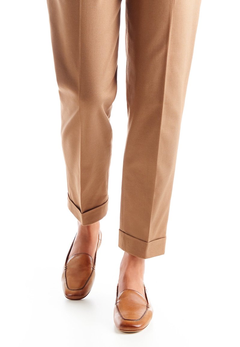Pantalon taillé marron avec ourlets repliés, associé à des mocassins en cuir marron clair avec un bout arrondi et des détails de couture.