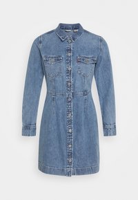 Modrá džínová košilová šaty s dlouhými rukávy, zapínáním na knoflíky vpředu, dvěma náprsními kapsami a mírně přiléhavým pasem. Texturovaná látka se švy.