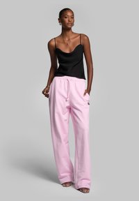 Sort silke camisole med tynde stropper parret med løse pink bomulds sweats, der har en elastisk talje og lommer.