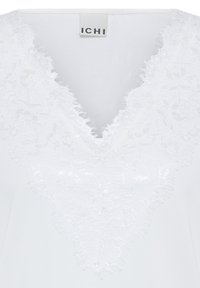 Haut blanc avec un décolleté en V profond orné d'une fine bordure en dentelle florale et de bords festonnés, étiqueté avec la marque "ICHI."