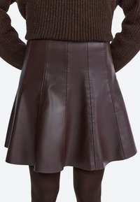 Brown leather flared skirt with pleats, featuring a smooth texture and a slightly shiny finish, paired with a knit sweater.
