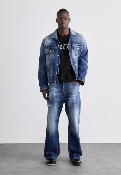 Denim-jakk, millel on heledam pesu ja kulumise detailid, koos lahtiste, tuhmide teksadega. Must sweatshiirts all, läikivad mustad kingad.