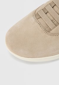 Bout de basket en daim beige avec lacets assortis et semelle en caoutchouc clair sur un fond blanc uni.