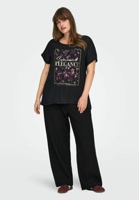 Musthave musta üleizee T-särk lillelise graafikaga, millel on kuldne tekst. Kombineeritud lõtvade mustade pükste ja tumepunaste kingadega. Ühtlane kangastekstuuri.