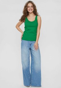 Grön linne med skopa halsringning, parat med ljusblå vida jeans. Outfitten har en mjuk textur och en avslappnad design.