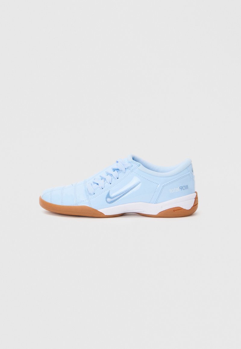 Tênis desportivo azul claro com um cabedal sintético liso, detalhes texturizados e uma sola de borracha tipo gum. Apresenta um logótipo na lateral.