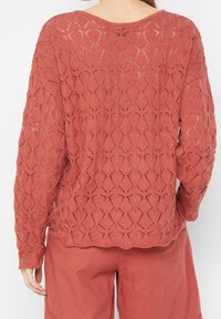 Suéter de punto en rosa empolvado con un patrón de encaje en diamante abierto. Mangas largas y un corte relajado. Tejido texturizado con detalles de costura visibles.