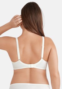 Witte beha met verstelbare bandjes, gladde stof en een haak-en-oogsluiting op de rug. Afgeronde naadloze cups zonder zichtbare patronen.