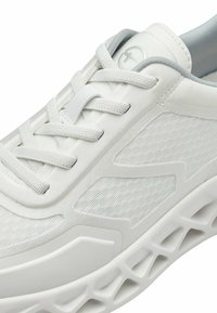 Valged sportlikud jalanõud, millel on võrgust ülemine osa, tekstureeritud disain, siledad sünteetilised kattekihtide ning eristuv kerge tald, millel on lõigatud aksendid.