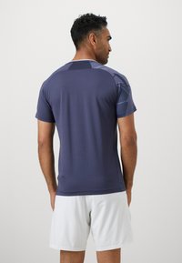Tricou sportiv bleumarin cu mânecă scurtă, cu o textură netedă, având un model geometric în nuanțe mai deschise pe umeri și spate.