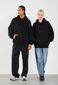 Sort oversized hættetrøjer med forsigtige lommer og snore til justering. Sorte track pants og lyseblå løst siddende jeans fuldender outfittet.