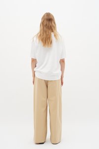 Hvid kortærmet t-shirt med afslappet pasform, parret med beige brede bukser. Glat tekstur, minimalistisk design, ingen synlige mønstre eller detaljer.