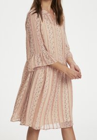 Robe douce rose à motifs floraux, avec des rayures verticales et des manches trois-quarts à volants. Col à boutons, silhouette évasée fluide.