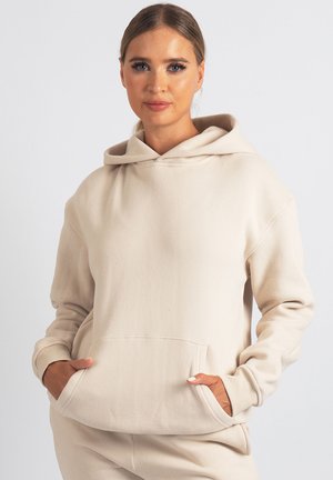 Beigen värinen ylivertainen huppari, valmistettu pehmeästä materiaalista, jossa suuri etutasku, kiristysnauhallinen huppu ja resorit hihansuissa.