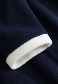 Navy blue fleece fabric with a soft, white, plush cuff. The texture is smooth and warm, highlighting the contrast between colors.