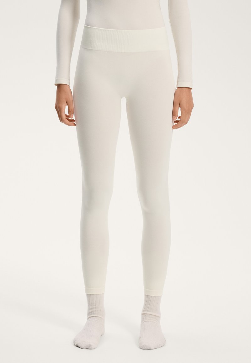 Leggings bianchi elasticizzati con una ampia vita a costine; texture liscia; lunghezza alla caviglia; abbinati a calzini bianchi alla caviglia.