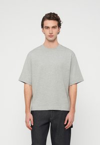 Γκρι βαμβακερό μπλουζάκι με κοντά μανίκια, στρογγυλή λαιμόκοψη και άνετη εφαρμογή. Το ύφασμα φαίνεται λείο και χωρίς ιδιαίτερα χαρακτηριστικά, χωρίς ορατά μοτίβα ή διακοσμήσεις.