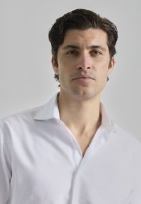 Camisa blanca de botones con una textura suave, que presenta un cuello clásico y un detalle de botones visible, exhibida sobre un fondo neutro.