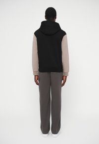 Sudadera con capucha negra con mangas beige, con capucha ajustable con cordón. Combinada con pantalones deportivos grises. Diseño simple y casual, textura suave.