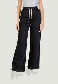 Pantalones de pierna ancha negros, hechos de tela texturizada, con cintura elástica y cordón. Incluye detalles en tono dorado.